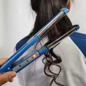 Plancha alisadora y rizadora 2 en 1 azul brillante Alizz Curling 480 con placas térmicas metalizadas moldeando un mechón de cabello ondulado